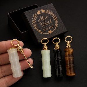 May include: Four small cylindrical vials with gold-toned metal caps and attached spoons, featuring bamboo-like textures in white, pale green, black, and brown stone. A black gift box displays the gold text Alice & David 08.15.2021 inside a wreath.
