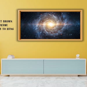 May include: A rectangular wall art piece featuring a vibrant spiral galaxy with a bright central core, encased in a light brown wooden frame. The text LIGHT BROWN FRAME READY TO HANG is printed in black on the left side of the wall art.