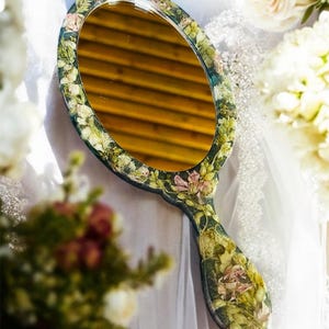 May include: A hand mirror with an oval-shaped glass surrounded by a floral design. The handle is also decorated with flowers and leaves.