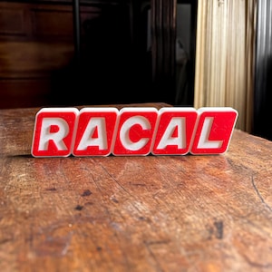 Könnte beinhalten: Nahaufnahme des Wortes "RACAL", das in weißen Buchstaben auf roten Blöcken geschrieben ist. Die Blöcke liegen auf einer Holzoberfläche.
