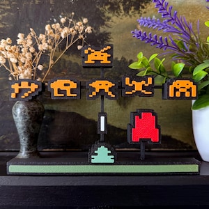 May include: A black and green pixel art sculpture featuring various retro video game characters. The sculpture includes orange and red pixelated figures, mounted on a black base with a green accent. The design is reminiscent of classic arcade games.