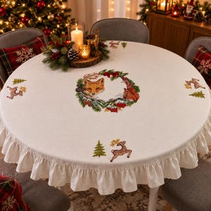 Könnte beinhalten: Eine runde, cremeweiße Tischdecke mit Rüschensaum, verziert mit gestickten Waldmotiven wie einem zentralen Kranz mit Fuchs und Eichhörnchen, Tannenbäumen und Hirschen. Der Stoff ist mit farbenfrohen Mustern im Waldthema gestaltet.