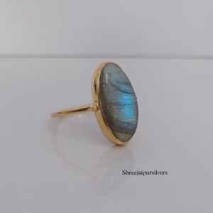 May include: A gold ring with a large oval-shaped labradorite gemstone. The gemstone has a blue-green iridescent sheen.