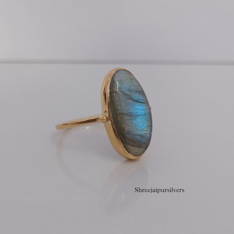 May include: A gold ring with a large oval-shaped labradorite gemstone. The gemstone has a blue-green iridescent sheen.