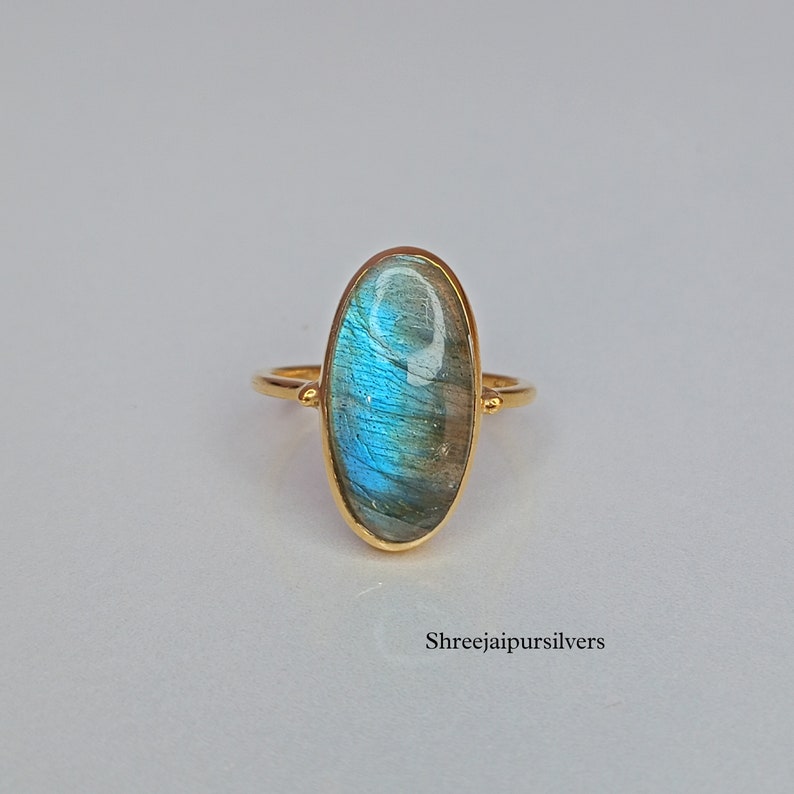 May include: A gold ring with a large oval-shaped blue labradorite gemstone. The ring is set in a simple gold band.