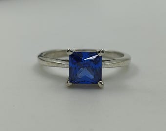 May include: A silver ring with a square-shaped blue gemstone.
