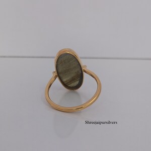 May include: A gold ring with an oval-shaped labradorite gemstone. The ring is simple and elegant, with a smooth band.