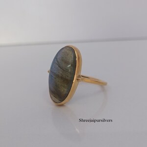May include: A gold ring with a large oval-shaped labradorite gemstone. The ring is set in a simple, modern style.