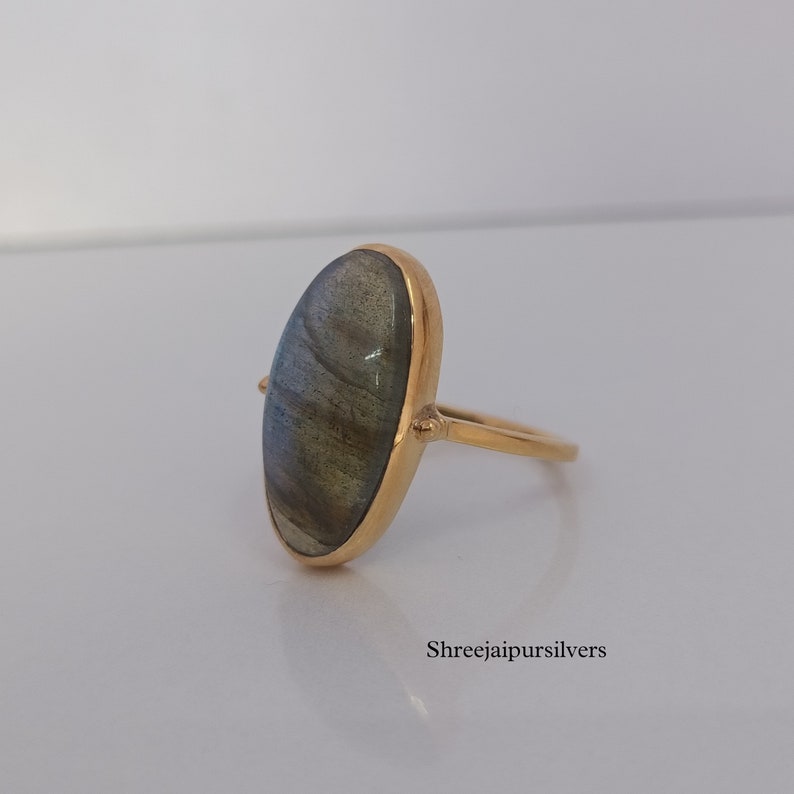 May include: A gold ring with a large oval-shaped labradorite gemstone. The ring is set in a simple, modern style.