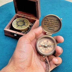 May include: A brass pocket compass with a hinged lid featuring the engraved quote, Go confidently in the direction of your dreams. Live the life you have imagined. - Thoreau. The compass includes a matching wooden storage box with a metal latch.