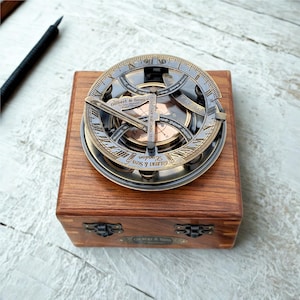 Peut inclure: Un cadran solaire en laiton avec un cadran circulaire portant des chiffres romains et l'inscription Gilbert & Sons London. L'instrument est fixé sur une boîte en bois carrée avec des loquets métalliques et une plaque en laiton Gilbert & Sons London.