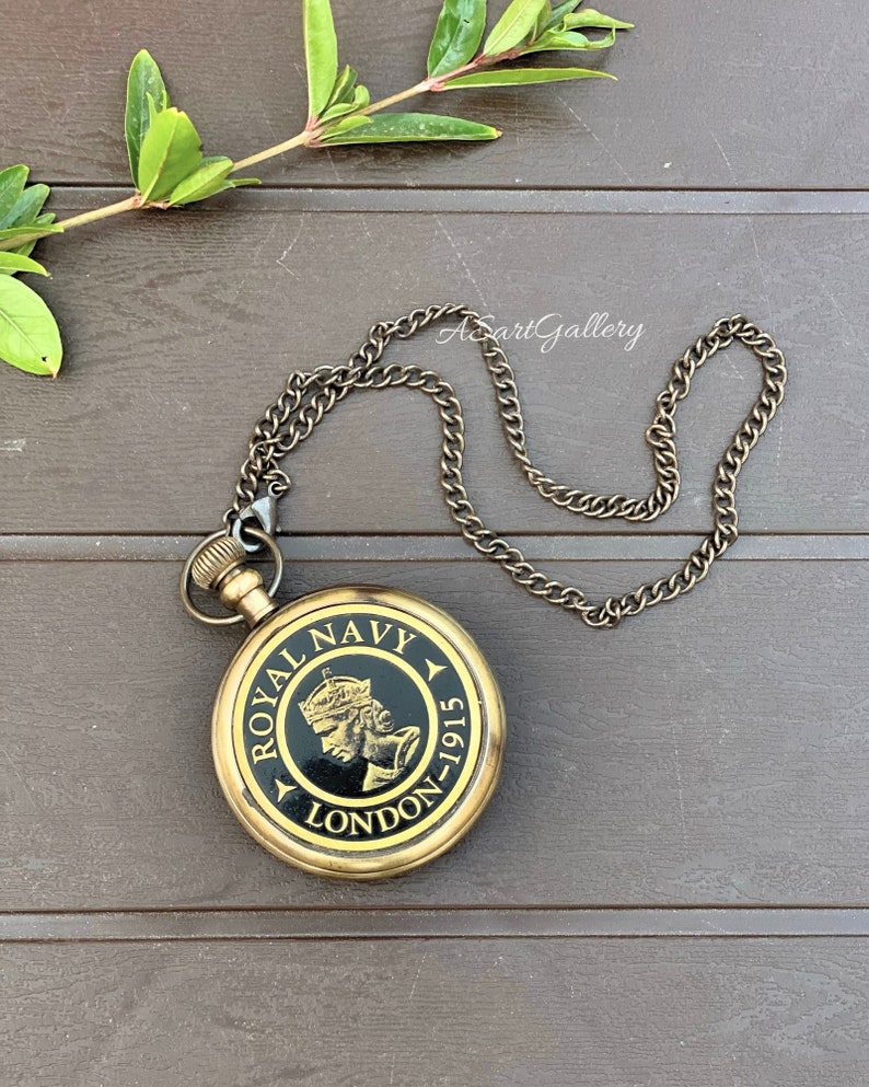 May include: A gold-toned pocket watch with a black face and a chain. The face of the watch has the words "Royal Navy London-1915" and a depiction of a crowned woman.