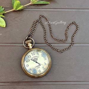 May include: A gold-toned pocket watch with a chain. The watch face has Roman numerals and says "Victoria London 1915".