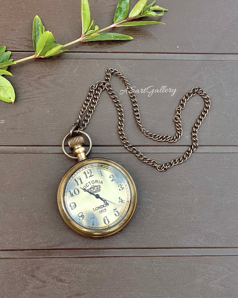 May include: A gold-toned pocket watch with a chain. The watch face has Roman numerals and says "Victoria London 1915".