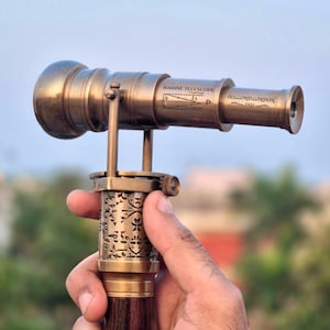 Detailed view of the antique brass telescope handle held in hand, showing fine artisanal engraving.