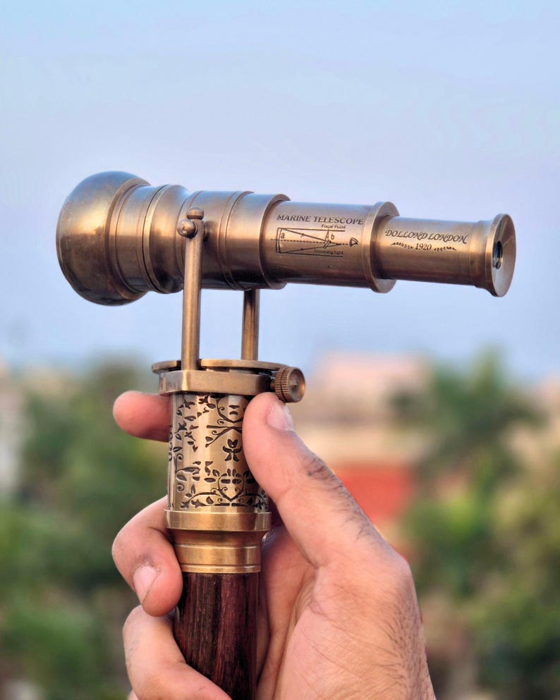 Detailed view of the antique brass telescope handle held in hand, showing fine artisanal engraving.