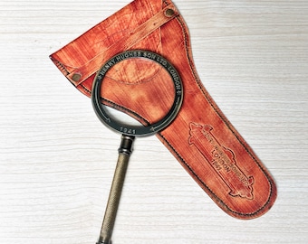 May include: A vintage magnifying glass with a brass handle and a leather case. The case is brown and has the inscription "X. Henry Hughes Son Ltd. London" on it. The magnifying glass has the inscription "1941" on it.
