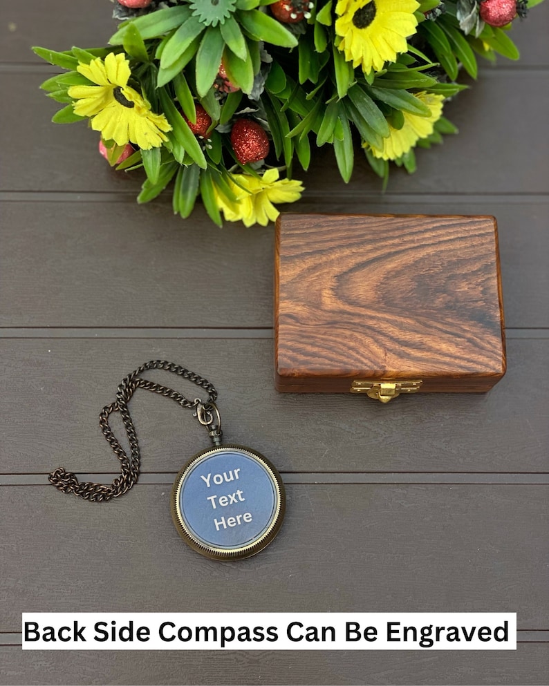 May include: A round antique-style compass with a dark metal chain and a blue face featuring the text Your Text Here, accompanied by a rectangular dark brown wooden box with a gold-toned metal latch, positioned near a bouquet of yellow flowers.