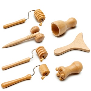 Könnte beinhalten: Satz mit sechs Holzmassagewerkzeugen, darunter eine Rolle, eine Tasse, ein Paddel und drei kleine Werkzeuge mit verschiedenen Texturen. Die Werkzeuge sind aus hellbraunem Holz gefertigt und für die Körpermassage konzipiert.