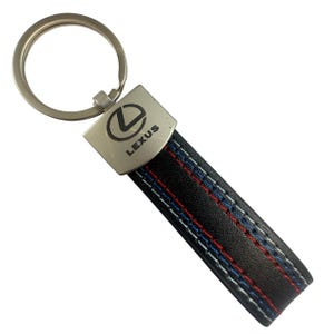 May include: Black leather Lexus keyring with red, white, and blue stitching. The keyring features a silver-coloured metal ring and a rectangular metal plate with the Lexus logo and the word "LEXUS".