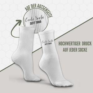 May include: Two white ribbed socks with the text "Coole Socke SEIT 1989" printed on them. The socks are displayed on a light gray background with additional text in German. The image highlights the high-quality print on each sock.