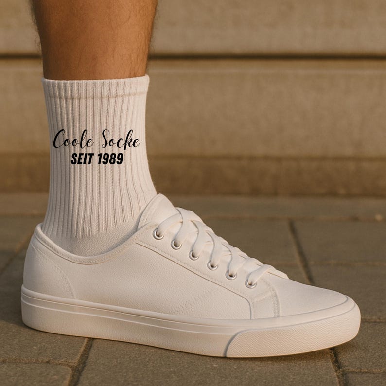 May include: White sneakers with white laces and a white sole. The image also shows a white sock with the text "Coole Socke SEIT 1989" in black script. The shoe is made of a smooth material.