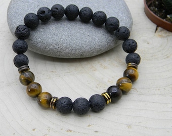 Puede incluir: Un brazalete de cuentas de lava negra y ojo de tigre. El brazalete tiene detalles dorados entre las cuentas.