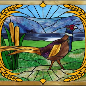 Puede incluir: Una ventana de vitral que representa un faisán de pie en un campo con hierba alta y juncos. El fondo muestra un lago y montañas. La ventana está enmarcada con un diseño de trigo.