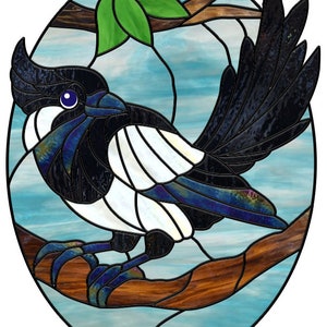Peut inclure: Une fenêtre en vitrail représentant une pie noire et blanche perchée sur une branche. L'oiseau a un œil bleu et est placé sur un fond de ciel bleu et blanc.