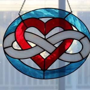 May include: A stained glass window hanging with a red heart intertwined with a white infinity symbol. The background is a blue-green color.
