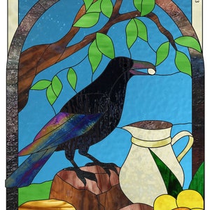 Peut inclure: Une fenêtre en vitrail représentant un corbeau noir perché sur un rocher, tenant une perle blanche dans son bec. Un pichet blanc avec une feuille verte se trouve à côté du corbeau, et une fleur jaune avec un centre orange est au premier plan. Le titre "The Crow & the Pitcher" est en haut de la fenêtre, et le nom de l'artiste "Carolyn Murie" est en haut à droite.