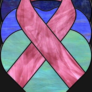 May include: A stained glass heart with a pink ribbon in the center. The heart is made of blue, green, and pink glass.
