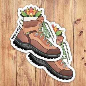May include: A brown hiking boot with green laces and a white sock. The boot is decorated with a small bouquet of autumn leaves and flowers. The text "Take a Hike" is written on the side of the boot.