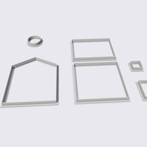 Op de afbeelding: Een set van zeven witte plastic koekjesvormen in de vorm van een huis, ramen en een cirkel.