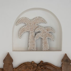 Può includere: Due palme bianche fatte di conchiglie sono esposte in una nicchia bianca in un muro. Le palme sono un'opera d'arte murale decorativa.
