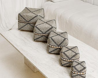 May include: Five gray and black beaded boxes of varying sizes, arranged in a row on a white marble surface. The boxes have a geometric pattern and are made of natural materials.