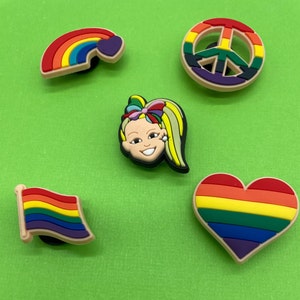 May include: Five colorful shoe charms featuring a rainbow, a peace sign, a heart, a rainbow flag, and a cartoon girl with blonde hair and a rainbow bow.