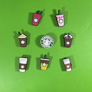 May include: Eight different Starbucks-themed shoe charms, including a green charm with the Starbucks logo and the words "Starbucks Coffee", a pink charm with a pink and white striped cup, a brown charm with a brown cup with whipped cream, a yellow charm with a yellow cup with a green straw, and four other charms with different colored cups.