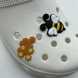 Puede incluir: Zapato blanco con una abeja negra y amarilla y un amuleto de panal amarillo y marrón.