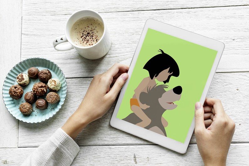 Puede incluir: Una tableta blanca con un fondo verde que muestra una imagen de dibujos animados de Mowgli del Libro de la Selva de Disney montando a Baloo el oso. La tableta est&aacute; siendo sostenida por las manos de una persona.
