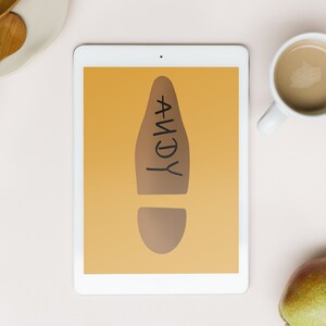 May include: A digital tablet displays a brown footprint graphic with the name "ANDY" in black. The tablet is on a light pink surface, accompanied by a cup of coffee and a pear.