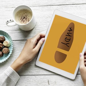 May include: A digital tablet displaying a brown footprint graphic with the name "ANDY" in black. A cup of coffee and a plate of assorted chocolates are on a white wooden surface.