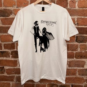May include: White t-shirt featuring a black and white image of Fleetwood Mac's "Rumours" album cover.