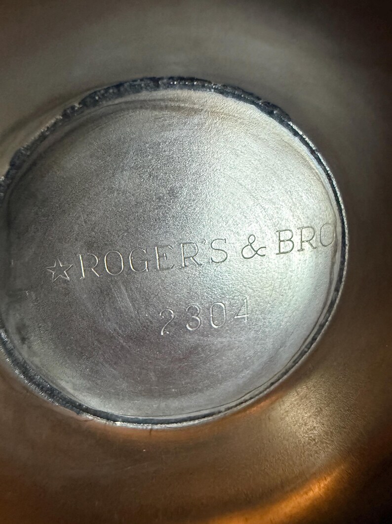 May include: Close-up of the interior of a silver-toned metal object. The text "ROGERS & BRO" is stamped in a curved line, with the number "2304" below. The metal has a slightly textured surface.
