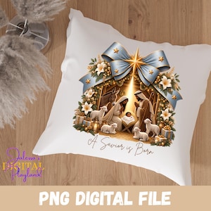 May include: A white square throw pillow featuring a nativity scene illustration with a large light blue bow, white lilies, and gold stars. The central graphic depicts figures, a donkey, and lambs around a manger with the text A Savior is Born.