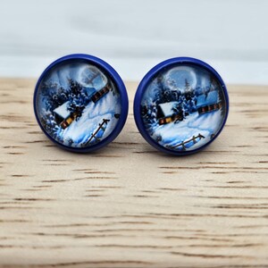 May include: A pair of blue and white glass earrings with a winter scene of a snowy village and a full moon.
