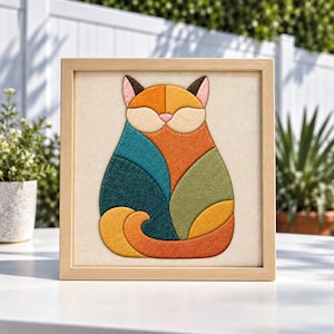 Puede incluir: Un cuadro cuadrado con una ilustración de un gato estilizado compuesto por parches de tela geométricos en tonos verde azulado, naranja, verde oliva y amarillo mostaza. El gato tiene cara beige claro, nariz rosa y fondo crema.