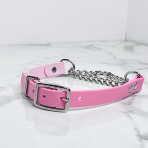 May include: A pink and silver collar with a chain and buckle closure. The collar is made of a soft, flexible material and features a silver chain and buckle. The collar is designed for pets.