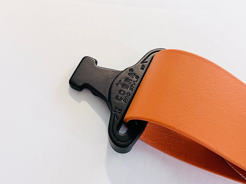 May include: Close-up of a brown leather strap with a black Cobra Pro Style buckle. The buckle has a small arrow pointing to the right and the text "7/8" above the Cobra logo.