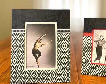 May include: Two decorative picture frames with black and white geometric patterns. One frame features a black and white photo of a male dancer. The other frame has a black and white photo of a woman in a winter scene.